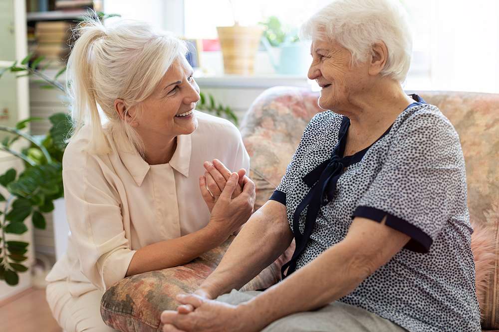 Senior woman smiles while holding hands with a caregiver in a senior living community.