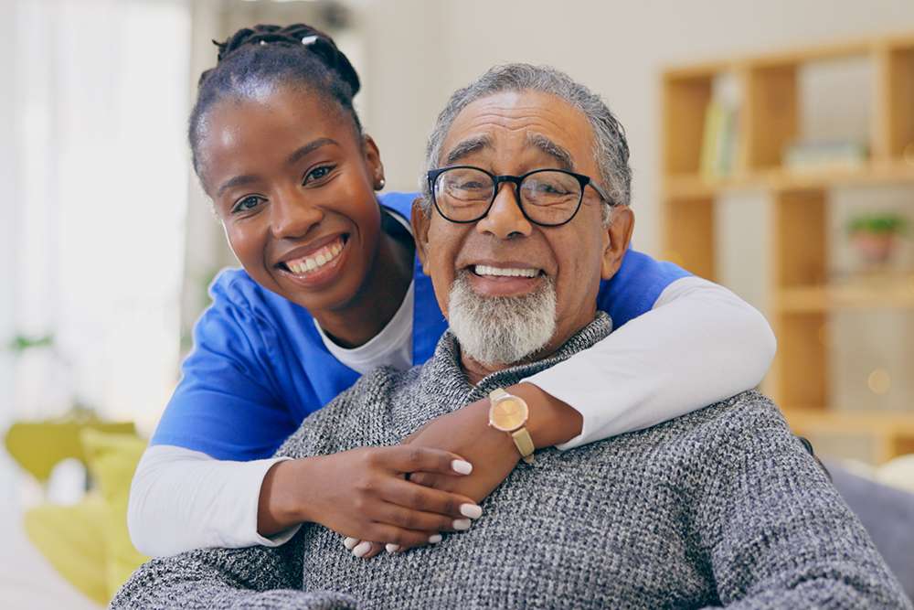 Caregiver hugging senior man, both smiling. Consider a senior living community for memory care.