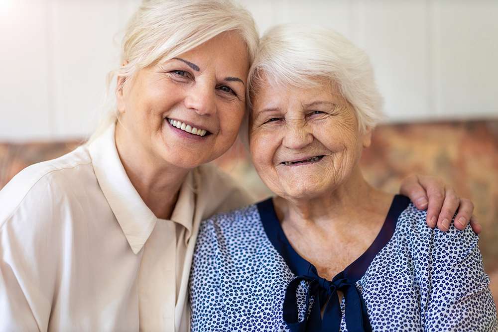 Smiling woman with arm around senior woman at senior living community