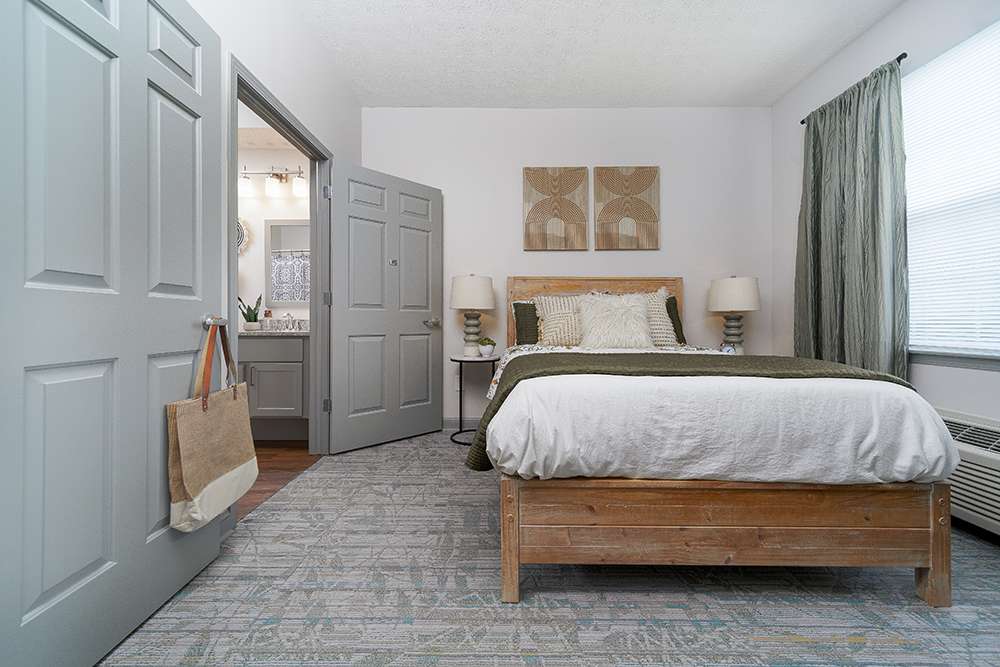 Bedroom in a senior living community with bed, rug, and open door to bathroom.